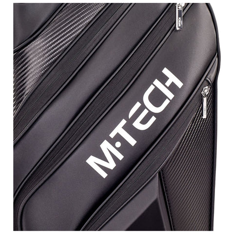 A black travel bag with a sleek design features zippers and carbon fiber accents showcasing the brand name M·TECH prominently displayed in white against the fabric surface.