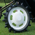 A black and white wheel with protruding spikes is positioned on grass suggesting use for outdoor tasks like gardening or landscaping with a device in motion nearby.