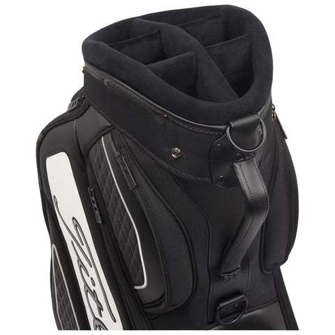 A black golf bag features a padded top with multiple compartments for club storage the bag has a sleek design with quilted fabric and contrasting white accents in a clean environment.