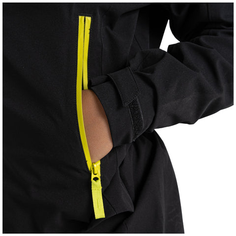 A black jacket with a bright yellow zipper is shown partially opened with a hand placing an object in the pocket the background is plain and uncluttered.