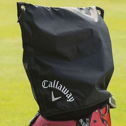 A black cover is draped over the top of a golf bag displaying the Callaway logo The bag sits on a grassy area likely at a golf course