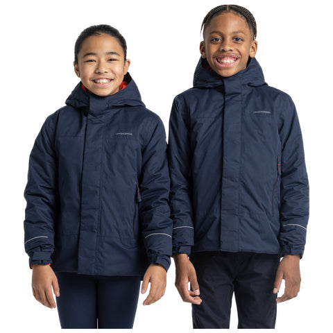 Two children are smiling while wearing matching navy blue jackets with hoods their hands are relaxed at their sides against a plain white background.