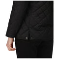 A black quilted jacket is partially unbuttoned revealing part of the wearer's hand and outlining the bottom hem while the wearer is positioned in a neutral setting.