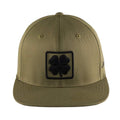 A green baseball cap featuring a black four-leaf clover patch on the front resting on a flat brim in an isolated setting.