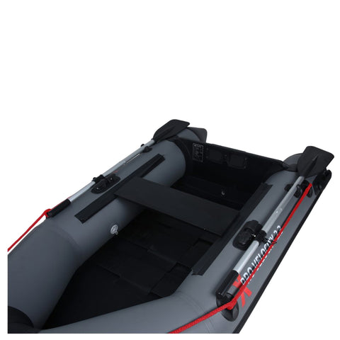 A gray inflatable boat rests on a flat surface featuring a black seating area and two oars attached at the sides while showcasing a simple design intended for recreational use.