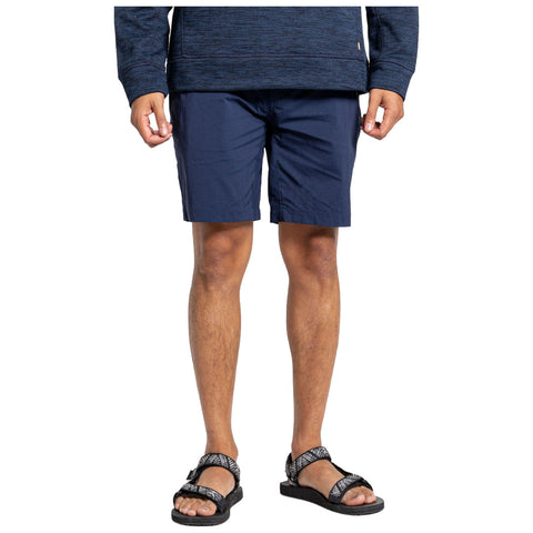 A person stands wearing a dark blue long-sleeve shirt and navy blue shorts paired with black sandals in a neutral setting. The individual appears ready for casual outdoor activities.