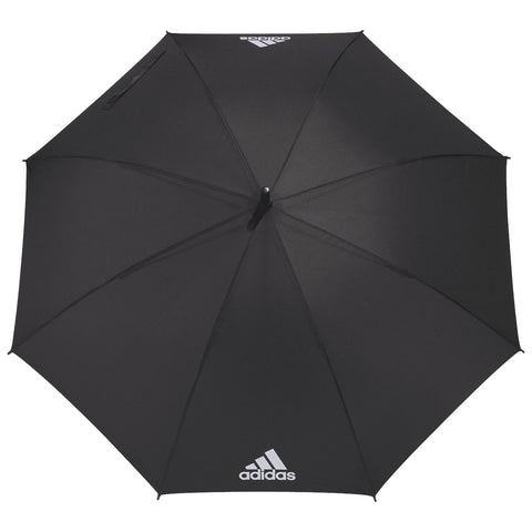 A black umbrella is opened wide displaying its smooth surface and a logo on one side while providing shade or shelter in an outdoor environment.