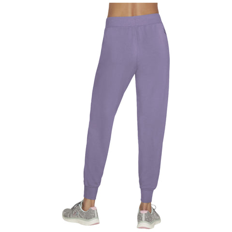 A pair of lavender sweatpants are worn by a person facing away from the viewer while standing on a flat surface the pants have a relaxed fit and cuffed ankles