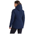 A woman wearing a dark navy jacket stands with her back to the viewer in a neutral background, showcasing the jacket's design and hooded feature.