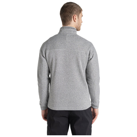 A person stands wearing a gray fleece pullover with a high collar their back is towards the viewer the background is plain emphasizing the clothing and posture