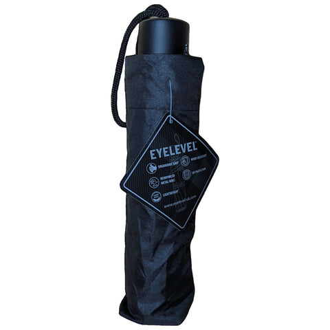 A black umbrella is standing upright with a carry strap and a tag attached. The umbrella is designed for functionality and durability with features like wind resistance and lightweight construction.