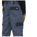 Gray work pants are displayed with cargo pockets visible on the sides the pants are being worn by a person with a black long-sleeve shirt in an unspecified environment.