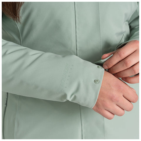 A mint green jacket is shown with a person fastening the cuff using snap buttons while the other hand adjusts the sleeve, emphasizing the fabric's flexibility and design. The text reads AQUADRY STRETCH.