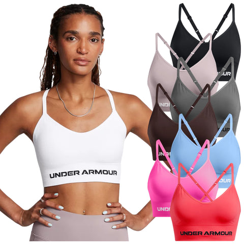 A woman is wearing a white athletic bra with 'UNDER ARMOUR' written on the band while standing confidently. Several colored bras in various shades are positioned around her against a plain background.