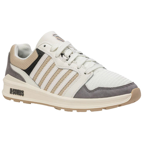 A sneaker is displayed featuring a combination of white and beige materials with grey accents and a textured mesh tongue laced tightly sitting on a light-colored sole in a neutral background.