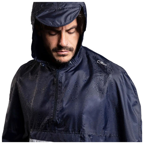 A man wearing a waterproof navy jacket stands still with water droplets on the fabric looking downwards in a neutral expression against a plain background.