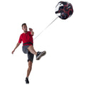 A man in a red shirt kicks a soccer ball attached to him by a cord while standing on a plain white background, focusing on improving his soccer skills.