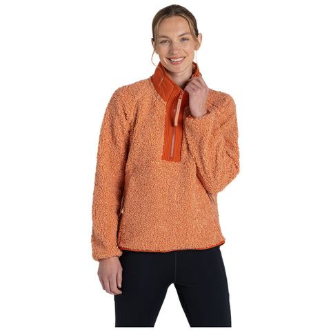 A woman stands smiling while wearing a bright orange fleece pullover with a zippered collar paired with black pants in a plain white background environment.