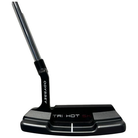 A golf putter with a sleek black design featuring the name "Odyssey" and "Tri-Hot 5K" is displayed standing upright against a plain background, showcasing its flat face and stainless steel shaft.