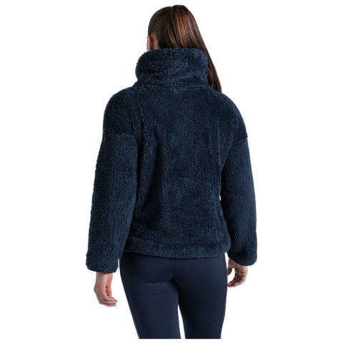 A person is standing with their back to the viewer wearing a dark navy fleece jacket with a high collar in a neutral setting, suggesting warmth and comfort.