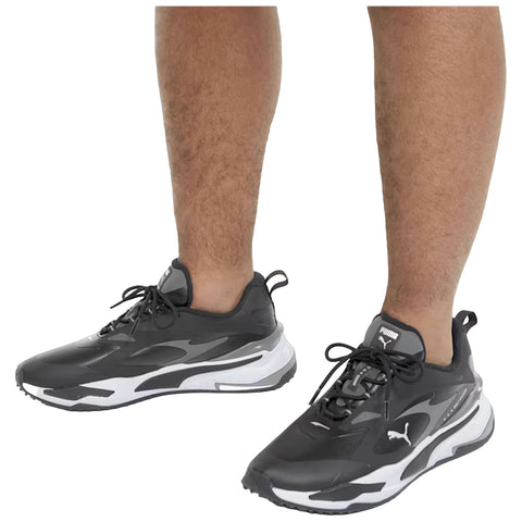 Black athletic shoes with white accents are positioned on a person's feet with visible legs exhibiting hair. The shoes appear sleek and modern, designed for comfort and style.