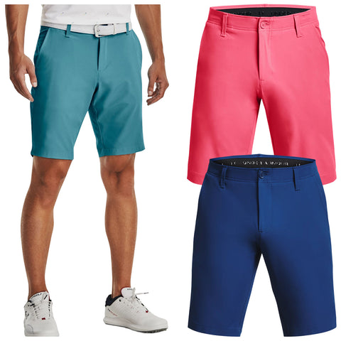 A man stands wearing teal shorts with a white belt while holding his hand on his hip. Two pairs of shorts in pink and navy are displayed alongside him.