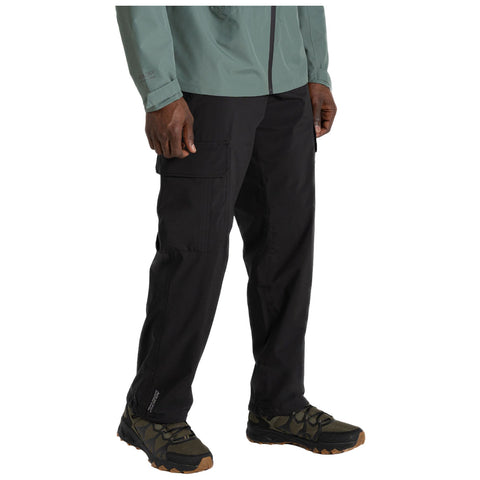 Black cargo pants are worn by a person standing with hands relaxed by their sides in a casual indoor setting, paired with green outdoor shoes and a light green zip-up jacket.