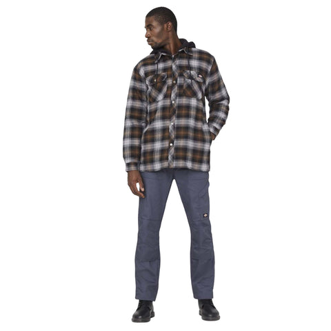 A man stands upright wearing a black and brown plaid flannel shirt over a dark hoodie paired with gray pants and black boots in a plain white background.