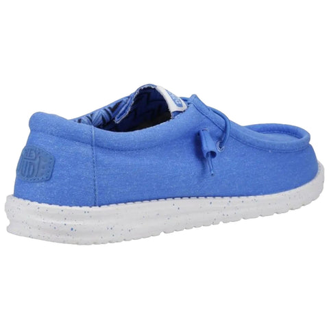 A blue slip-on shoe rests on a flat surface displaying a textured white sole the shoe features a looped string for tightening and a soft fabric upper with a patterned interior.