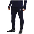 A person is wearing navy athletic pants and black soccer cleats while standing. The outfit features a visible logo on the thigh and is suitable for sports or training activities.