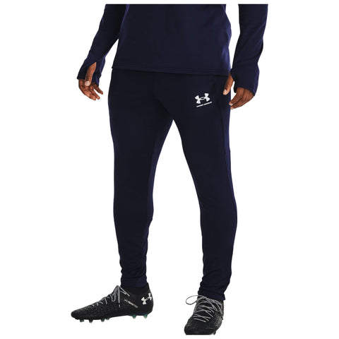 A person is wearing navy athletic pants and black soccer cleats while standing. The outfit features a visible logo on the thigh and is suitable for sports or training activities.