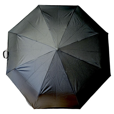 A black umbrella is open and resting flat with its fabric smooth and unwrinkled while a handle is positioned on one side against a plain background.