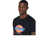 A man wearing a black t-shirt with a blue and red circular logo stands facing the camera. The shirt features the brand name Dickies and the phrase Hard Working Since 1922.