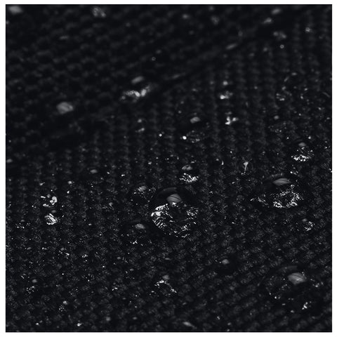 A textured black fabric is covered with small water droplets reflecting light while resting on a flat surface in a potentially dimly lit environment.