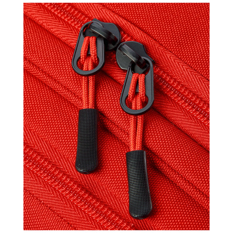 A close-up view of red fabric shows two black zipper pulls attached to a zipper track surrounded by textured material indicating it belongs to a bag or suitcase.