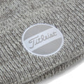 A knitted gray beanie features a circular logo with the name Titleist displayed in cursive against a background of two horizontal stripes in light gray and white.