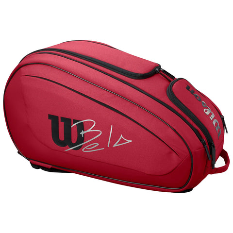 A red sports bag is resting on a flat surface featuring a prominent logo and signature design elements indicating its purpose for carrying sports equipment usually tennis rackets and gear.