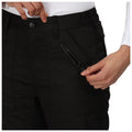 A hand holds the zipper of a pocket on dark pants while another hand adjusts the waistband in a neutral setting, showcasing a casual clothing style.