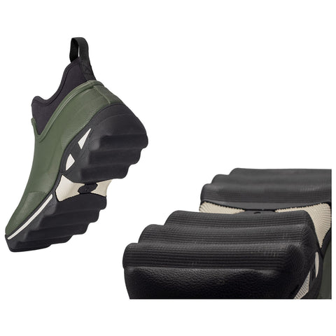 A green sneaker is elevated above the ground showcasing a thick black sole with indented patterns the background is plain emphasizing the shoe's design and texture.