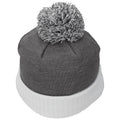 A knitted beanie with a gray body and white ribbed cuff sits upright featuring a fluffy gray pompom on top in a neutral setting without any distinct background elements.