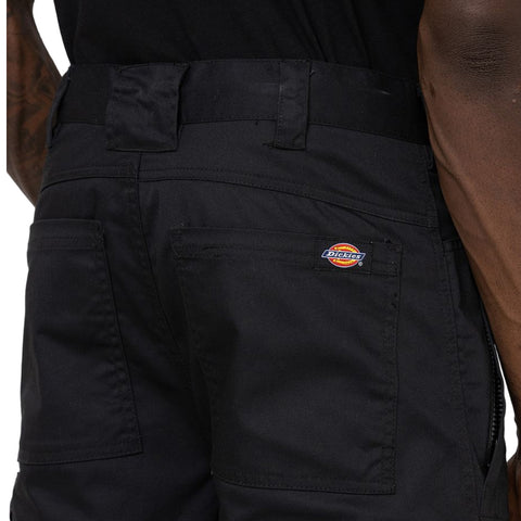 Black work pants are displayed with a visible logo on the back pocket indicating the brand Dickies. The clothing is styled for practicality in a labor-oriented context.