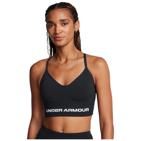 A woman is wearing a black sports bra featuring the brand name UNDER ARMOUR prominently displayed. She has long braided hair and is standing against a plain background.