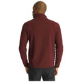 A man stands with his back to the viewer wearing a burgundy fleece jacket. The setting is neutral, emphasizing the clothing and the figure's silhouette.