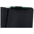 A black notebook is open with a green pencil resting on its edge secured by an elastic band indicating it is ready for note-taking in a simple workspace.