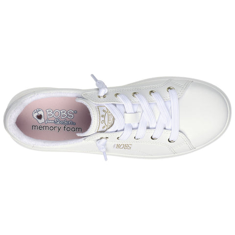 A white sneaker with laces and a logo inside rests on a flat surface emphasizing its clean design and comfort features in a casual footwear context. The insole reads BOBS from Skechers memory foam.