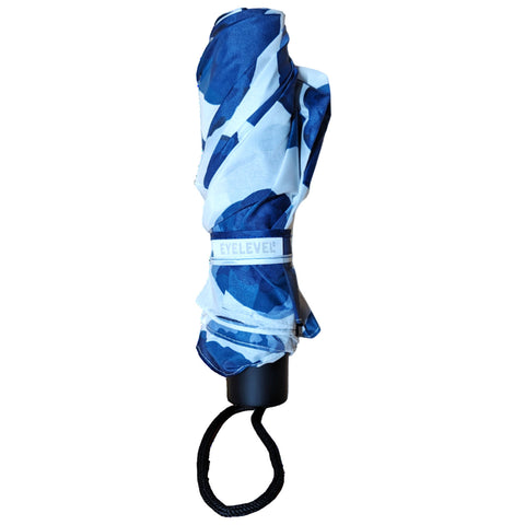 A closed umbrella is wrapped in a blue and white patterned fabric and secured with a strap labeled EYLEVEL. It is positioned upright against a plain white background.