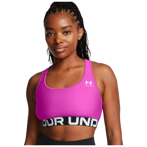 A person is wearing a bright pink sports bra with a black band featuring the text "UNDER" while displaying a confident expression against a plain white background.