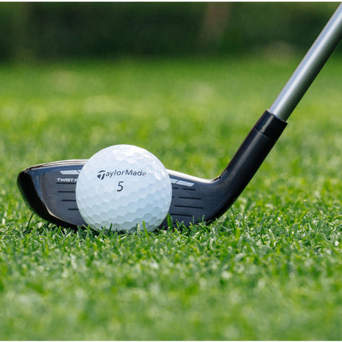 A golf club rests on green grass next to a white golf ball marked with the brand name TaylorMade and the number 5 ready for a shot.