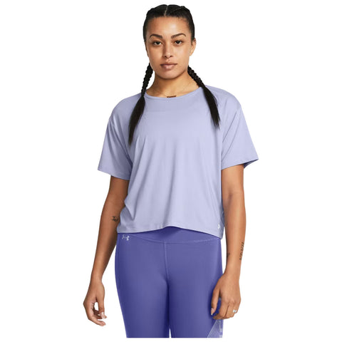 A woman with braided hair stands confidently wearing a light purple short-sleeve shirt and matching leggings in a neutral background, showcasing a casual athletic outfit.