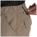 A hand is pulling a waistband toggle on a pair of khaki shorts featuring side pockets and detailed stitching in a neutral-toned setting that emphasizes the garment's functionality.